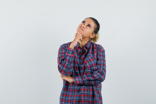 思考身穿格子衬衫的年轻女子站在思考的姿势 手放在下巴上 面带沉思 俯视前方健康成人女性