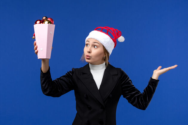 成功前视图年轻女性手持蓝色背景的圣诞树玩具新年假期女性蓝色人商人前面