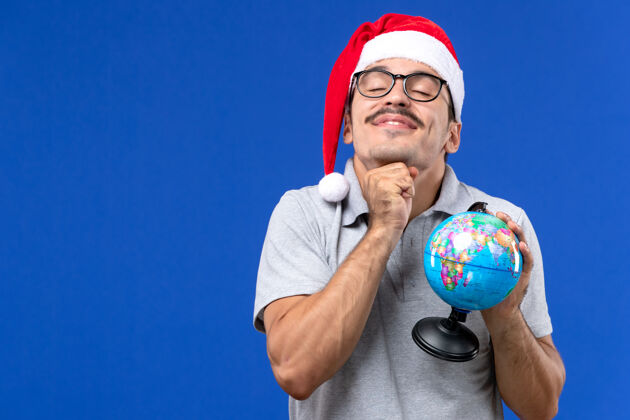 举行正面图年轻的男性手持地球仪在蓝色的墙壁旅行飞机度假男性地球仪圣诞节成人