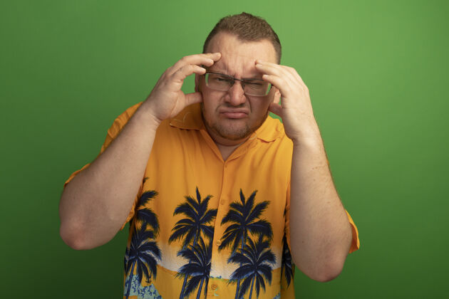 困惑一个戴着眼镜 穿着橘色衬衫的男人站在绿色的墙上 双手举过头顶 感到困惑和焦虑焦虑眼镜手