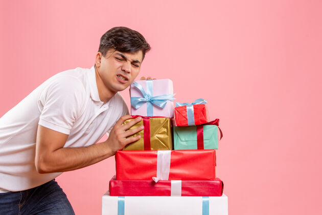成人正面图：年轻男性站在粉色背景的圣诞礼物周围前面观看举行