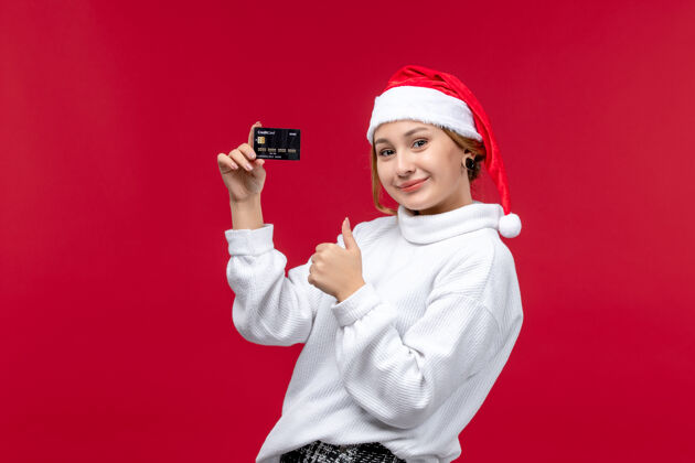 人正面图年轻女性手持红色背景的黑色银行卡红帽子圣诞节