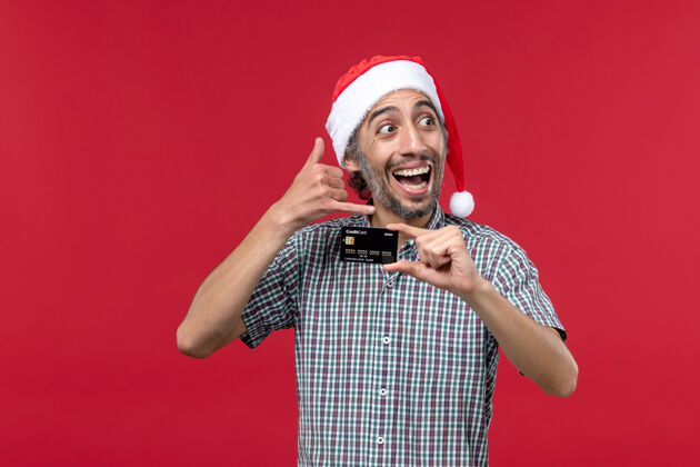 持有正面图年轻男子手持红色背景的黑色银行卡圣诞红银行