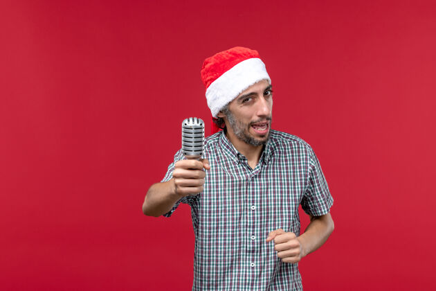 人正面图年轻男性手持麦克风 在红色背景上唱歌麦克风前面圣诞