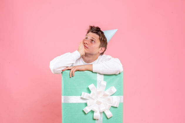 礼物正面图：身穿白色衬衫 头戴鸭舌帽的年轻男性 在粉色背景上呈现思考礼物白色正面