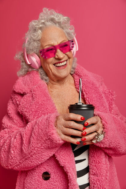 享受快乐满脸皱纹的老太太喝咖啡去 戴着耳机听音乐声音科技外套