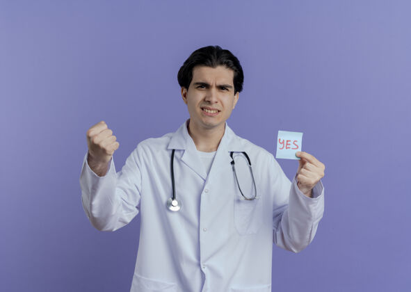 手势自信的年轻男医生穿着医用长袍和听诊器 显示是的 注意到正在做一个强烈的手势 隔离在紫色的墙壁上 有复制空间听诊器男性年轻