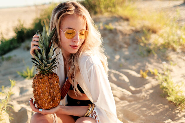 白天生活方式户外图片笑美丽的女人与多汁菠萝放松在阳光明媚的海滩时尚的夏季服装味道乐趣菠萝