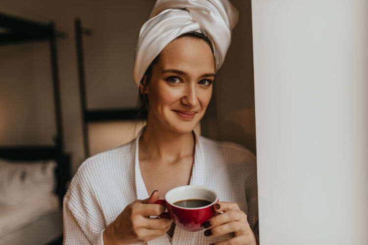 护理可爱的女人的肖像 脸上有胎记 穿着浴衣和毛巾 手里拿着一杯咖啡干净窗户长袍