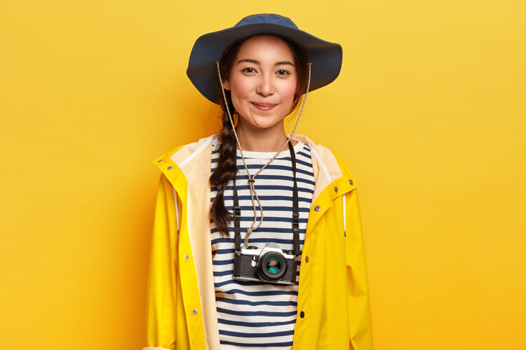 模特有才华的女摄影师在冒险之旅中进行专业拍摄 使用复古相机 戴时尚帽子 穿黄色雨衣 享受假期年轻人服装爱好