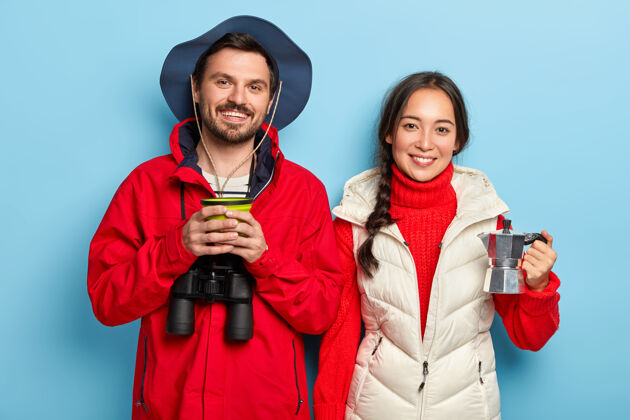 韩国这对幸福的夫妇在大自然中度过周末 喝咖啡 享受新鲜空气 用望远镜 穿着暖和的休闲服 站在蓝色的墙上 彼此挨着旅游咖啡自然