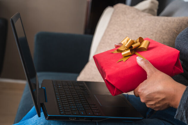 惊喜一个女人拿着一个红色礼品盒在她的笔记本电脑前的特写镜头技术女士笔记本电脑