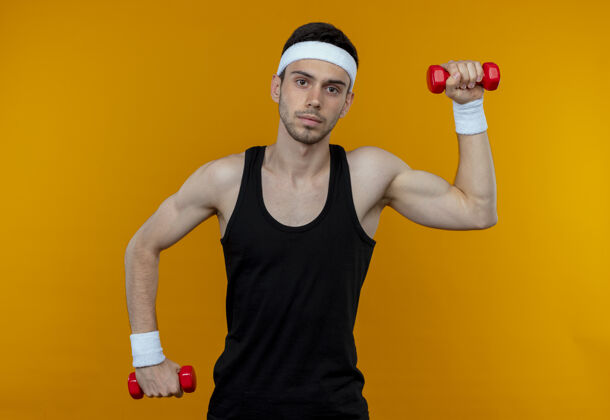 工作戴着头巾的年轻运动型男子 带着哑铃锻炼 严肃的脸庞凌驾于橙色之上男人运动哑铃