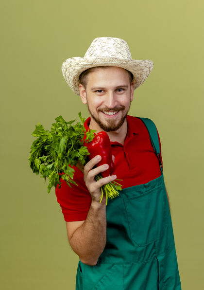 制服面带微笑的年轻英俊的斯拉夫园丁 穿着制服 戴着帽子 手里拿着香菜和胡椒粉微笑期待香菜