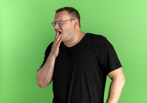 疲倦一个戴眼镜的胖男人穿着黑色t恤 看起来很累 打着哈欠绿色戴着看起来