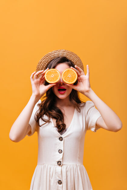 化妆穿着白色裙子和帽子的女孩的肖像 用橙色的两半遮住眼睛卷发裙子脸