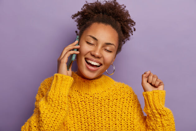 电话一位非洲裔女士在电话里交谈 谈吐有趣 举起紧握的拳头 在紫色的背景下露出与世隔绝的笑容女人玩耍满意
