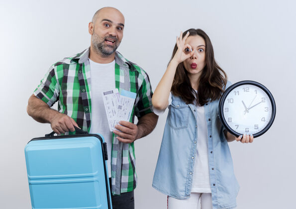 两者令人印象深刻的成人旅行者夫妇男人拿着手提箱和旅行票 女人拿着时钟 做着看的手势 两人都在看手提箱印象假期