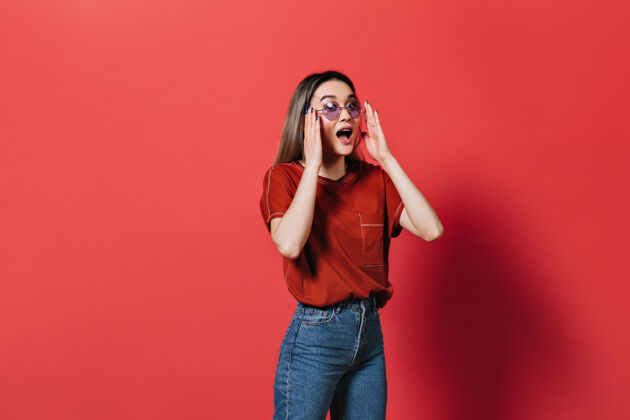 亚洲人一个戴着淡紫色眼镜 穿着红色t恤的女人在孤零零的墙上情绪化地摆姿势年轻跳跃室内