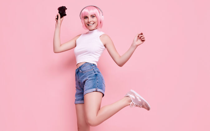 小玩意美丽快乐的游戏女孩与粉红色头发的肖像玩游戏机上五颜六色的操纵杆在工作室玩家霓虹灯疯狂