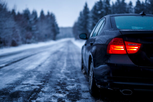 寒冷一辆黑色的车停在冰雪覆盖的道路上轮胎闪亮树