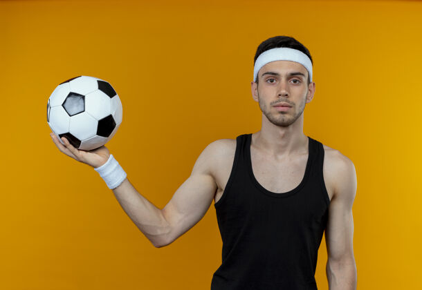 球戴着头巾的年轻运动型男子拿着足球站在橙色的墙上 表情自信严肃表情头带站着