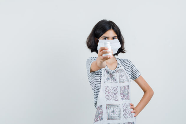 童年穿着t恤 围裙的小女孩展示着一瓶药片 看上去很自信 药丸自信瓶子