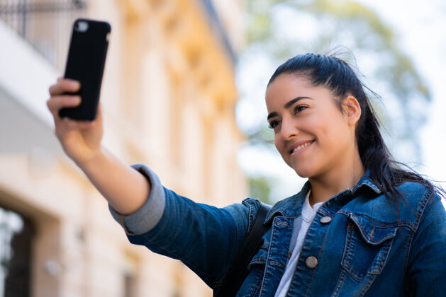 姿势年轻女子站在户外用手机自拍的照片手机聪明时尚