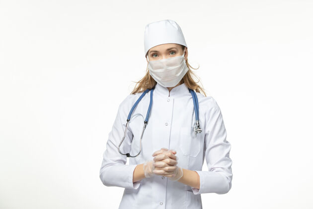 视图正面图女医生穿着医疗服 带着无菌口罩 因冠状病毒在浅白墙上传播疾病大流行性疾病冠状病毒-冠状病毒预防正面疾病