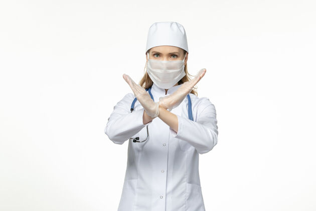 视图正面图女医生身穿医疗服戴口罩因冠状病毒显示禁止标志白墙病冠状病毒-大流行病毒病人员医生冠状病毒