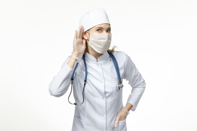 病毒前视图女医生穿着医疗服戴着口罩和手套试图听到轻壁病毒的冠状病毒-大流行疾病医疗疾病冠状病毒