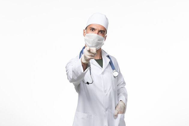 医疗正面图：男医生身穿防毒服 戴着防毒面具 指着白墙上的冠状病毒病大流行病毒病毒面具男性