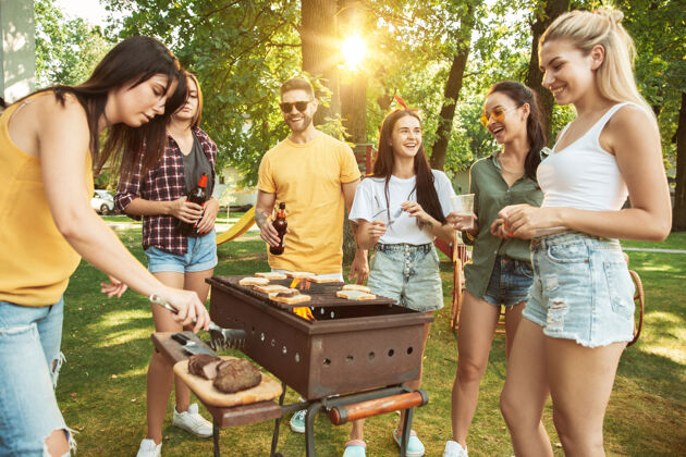 花园一群快乐的朋友在阳光明媚的日子里喝着啤酒 一起烧烤一起在户外的林间空地或后院休息午餐女人周末