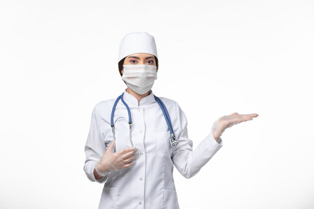 听诊器前视图：女医生穿着白色无菌医疗服 戴着口罩 因为白壁病毒-病毒-病毒-大流行性疾病冠状病毒防护病毒套装