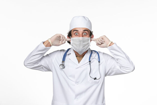 护目镜正面图：男医生穿着医疗服 戴着口罩 用白色办公桌上的冠状病毒大流行药物保护耳朵不受感染面罩冠状病毒病毒