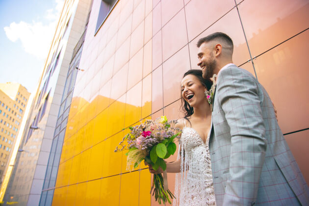 新郎高加索浪漫的年轻夫妇在城市里庆祝结婚温柔的新娘和新郎在现代城市的街道上家庭 关系 爱情的概念礼服婚礼花