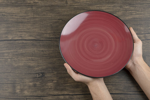 干净顶视图：男人的手拿着一个空的红色盘子放在木桌上盘子干净洗碗机