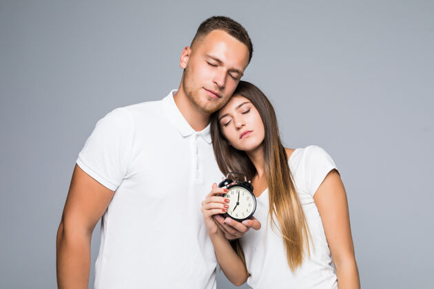 女孩一对年轻夫妇拿着闹钟 穿着白T恤 累极了电脑朋友女性