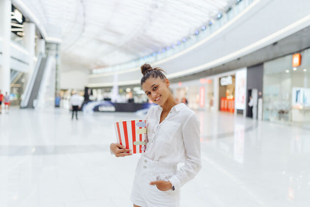 桶年轻可爱的女人拿着爆米花在商场的背景乐趣爆米花电影