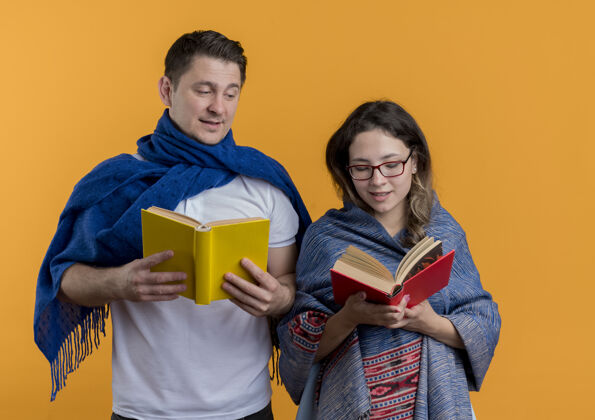 夫妻一对年轻夫妇拿着毯子拿着书幸福而积极地微笑着站在橙色的墙上抱着微笑积极