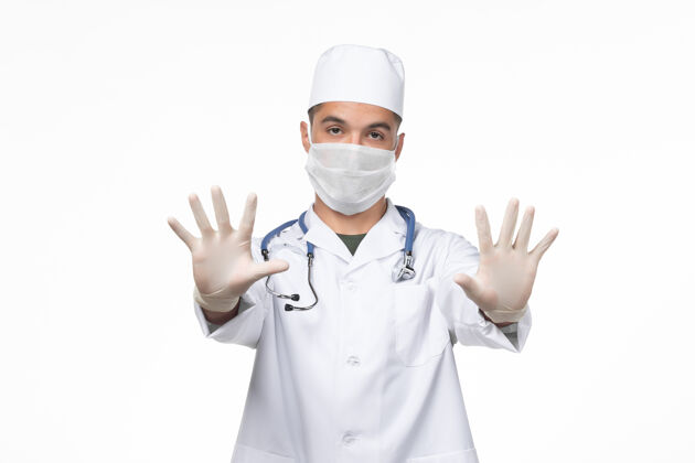 医生正面图：男医生穿着医疗服 戴着防冠状病毒口罩 在白墙上隔离冠状病毒疾病大流行人呆在家里面具