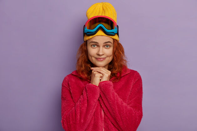 脸漂亮的女人双手合十 戴着黄色的帽子和红色的外套 直视镜头 脸颊上有酒窝滑雪者很活跃高兴一个女人