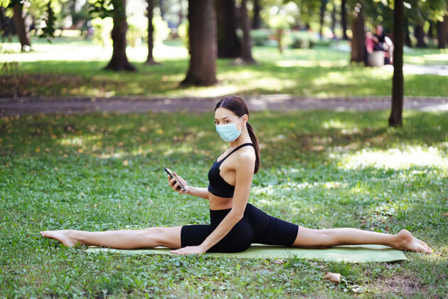 病毒戴着医用防护面具的运动型年轻女子 在公园里做瑜伽训练防护女人
