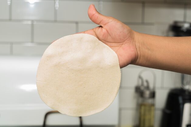 配料一个人拿着一个薄薄的圆面团在厨房灯光下特写面包师面粉人