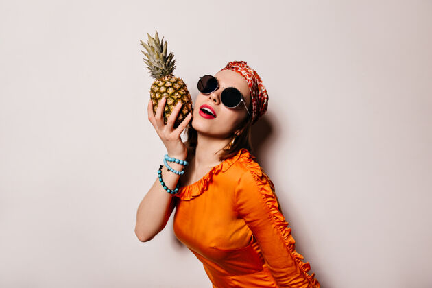剪戴着太阳镜 穿着橙色上衣的年轻女子在与世隔绝的空间里与菠萝合影的肖像女士酷菠萝