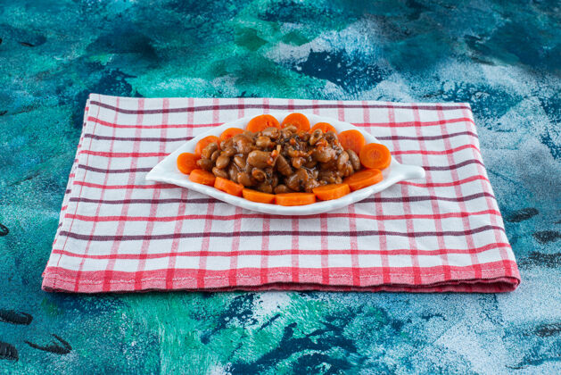 茶巾把胡萝卜和豆子片放在盘子里 把茶巾放在蓝色的盘子里盘子烘焙豆类