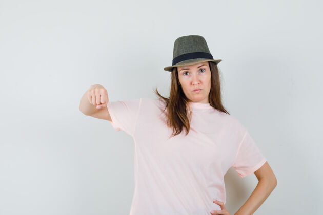 积极年轻女性穿着粉色t恤 戴着帽子 用拳头威胁 表情严肃正面视图帽子拳头肖像