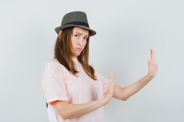 快乐年轻的女性穿着粉色t恤 戴着帽子举手自卫 表情严厉 正面照严格肖像帽子