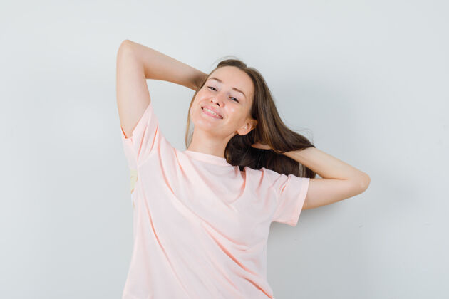 年轻年轻女性手挽着粉色t恤的头发摆姿势 看起来很迷人 正面照成人肖像时尚