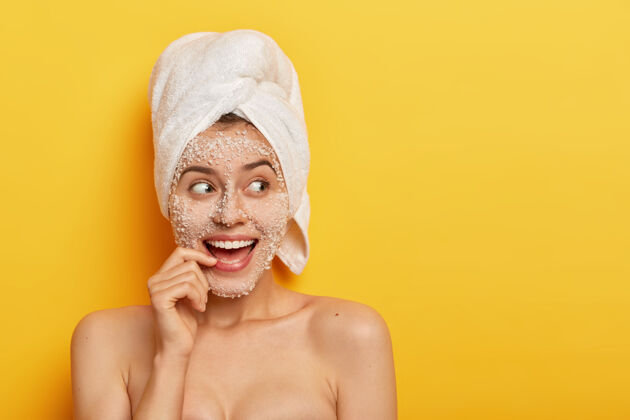 清洁快乐的欧洲女孩的照片 带着牙齿般的微笑 用海盐做spa 洗澡 拥有光滑健康的皮肤 目光移开 穿着白色毛巾 隔离在黄色背景上美丽的概念微笑裸体皮肤护理